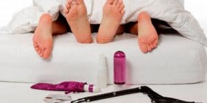 pies descalzos en una cama y juguetes sexuales tirados en el piso